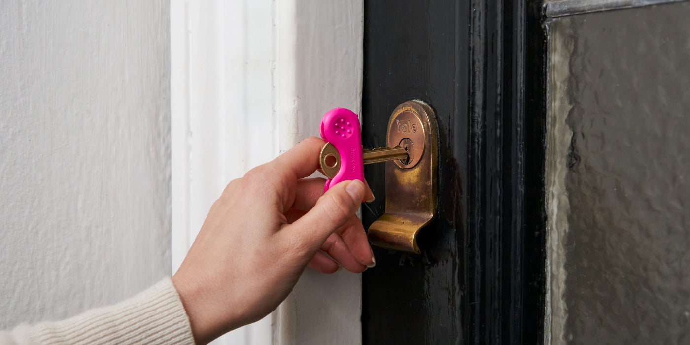A pink keywing key turner arthritis aid insertin key into a black door.