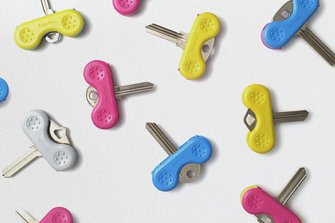 Scattered Keywing key turners on a white table on a range of keys. The Keywing key turners are blue, yellow, pink and grey and make the keys very easy to find.