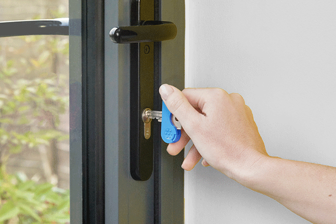 Blue keywing key turner arthritis aid use in a grey door to turn a key into a thumb turn.